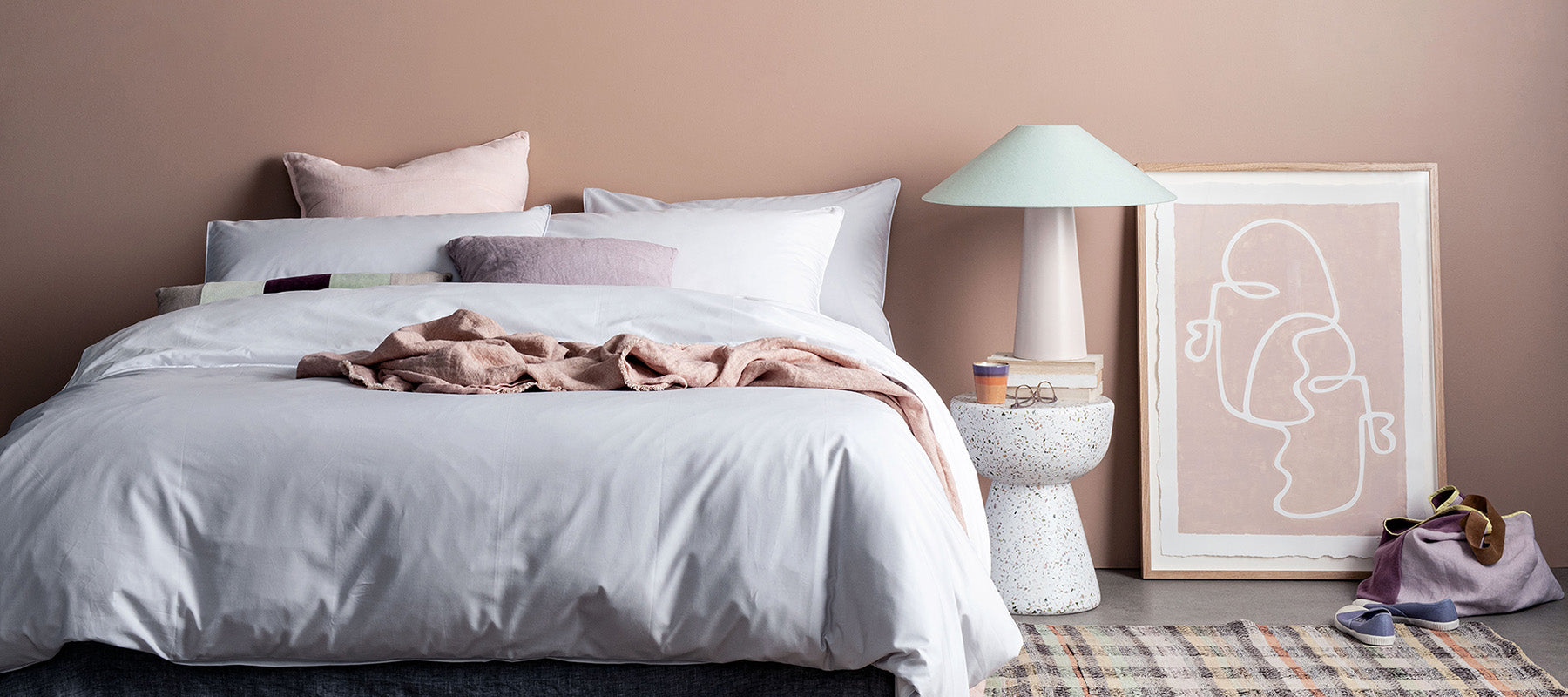Schlafzimmer mit feiner grauer bettwäsche aus weichem tencel stoff. hautfarbene wand und diverse dekor artikel neben dem bett