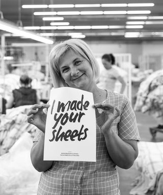 Frau in produktion aus portugal hält zeichen mit "I made your sheets"