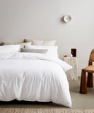 helles schlafzimmer mit weisser bettwäsche aus hoher qualität in tencel mit rattan stuhl und marmor tisch