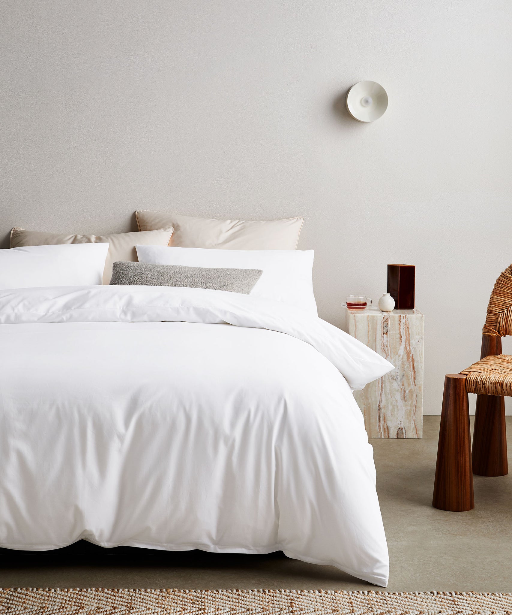helles schlafzimmer mit weisser bettwäsche aus hoher qualität in tencel mit rattan stuhl und marmor tisch